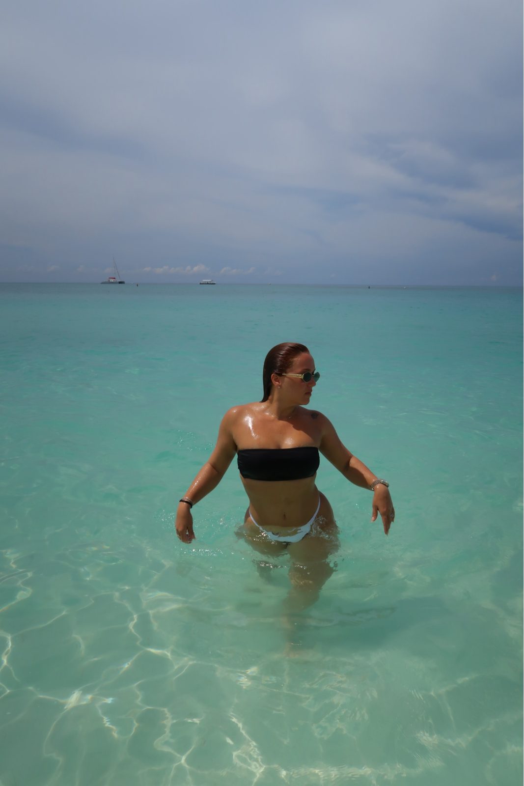 Berly wading into clear turquoise water in a black and white bikini